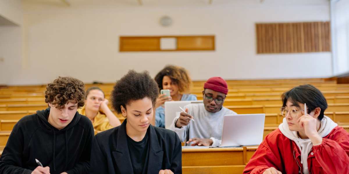 A diverse group of university students taking notes and using laptops in a lecture hall, illustrating student finance funding years in Scotland, Wales, and Northern Ireland.