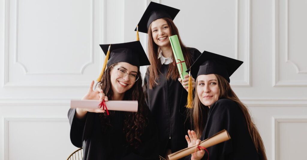 `Three female graduates smiling and holding diplomas after completing UK funded university degrees`