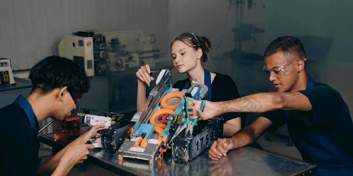 Three young apprentices wearing safety glasses working together on an engineering and robotics project in a workshop, illustrating what a degree apprenticeship looks like in practice.