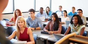 A diverse group of university students sitting at their desks in a lecture hall, listening attentively during a university class.