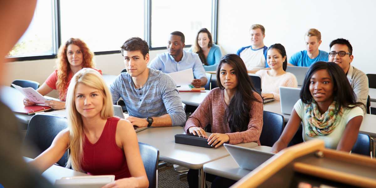 A diverse group of university students sitting at their desks in a lecture hall, listening attentively during a university class.