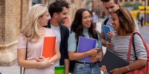 A diverse group of five happy university students smiling and celebrating outdoors on a bright day in a London city square, holding notebooks and binders, capturing a vibrant urban campus life atmosphere.