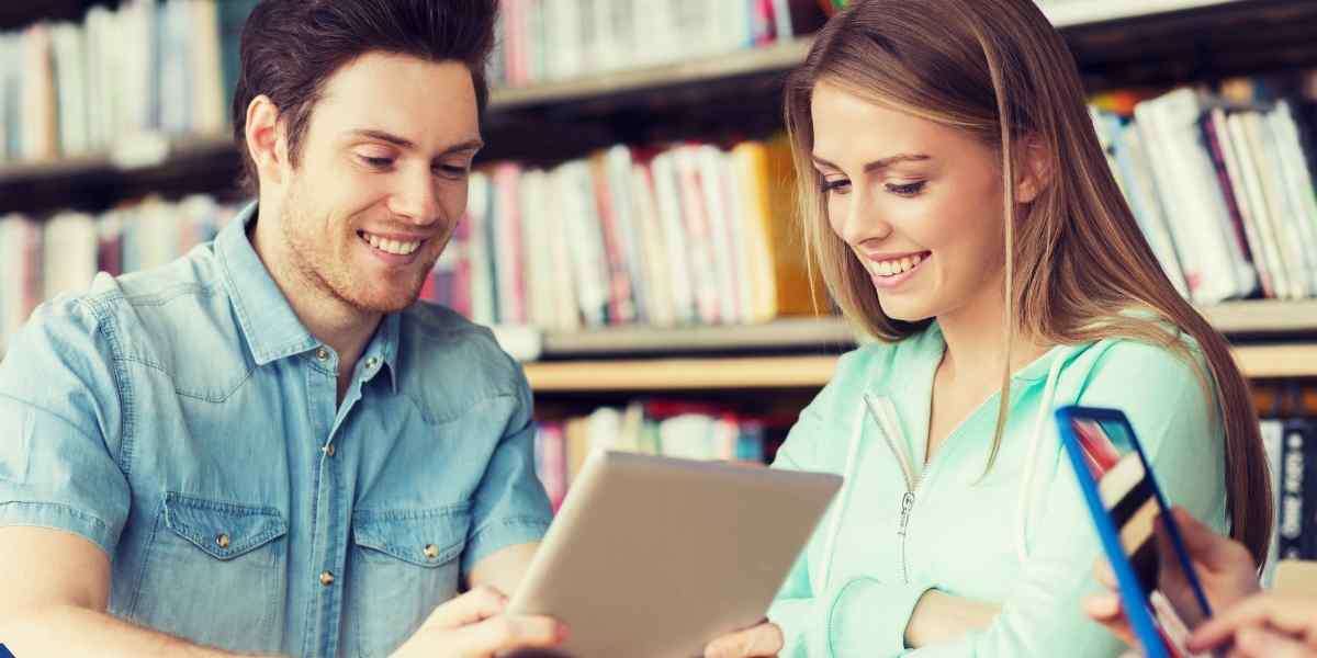 Two happy university students using a digital tablet in a library to read the complete guide on how to apply for Student Finance England 2026/27.