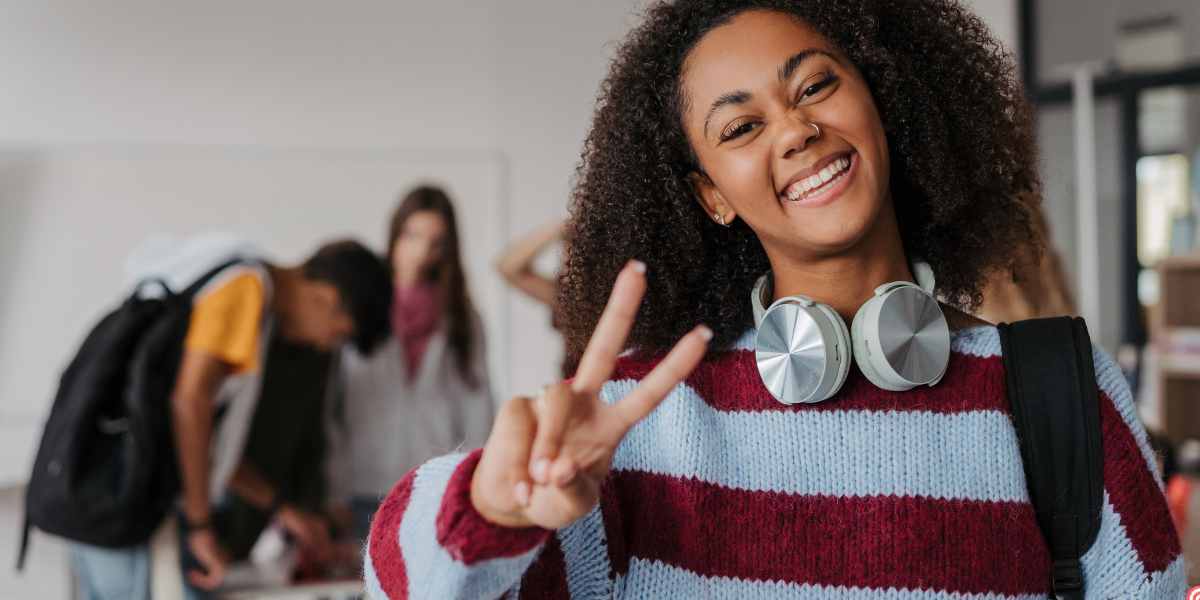 A smiling student with headphones making a peace sign, relieved after submitting her student loan application before the deadline.