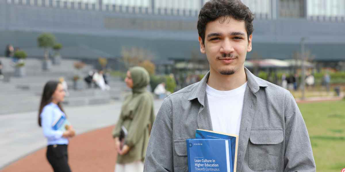 A young male university student holding textbooks outdoors on a campus courtyard, representing independent students navigating their Student Finance England application without parental support.