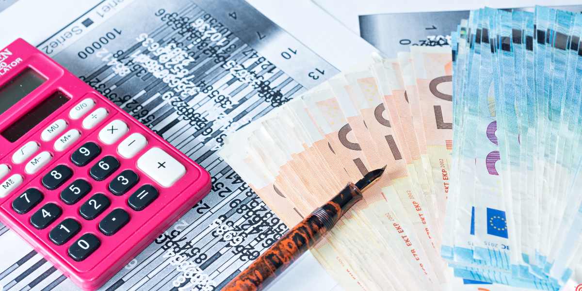 A high-angle view of European bank notes, a fountain pen, and a pink calculator resting on financial documents, representing student finance planning and checking eligibility for UK foundation year funding.