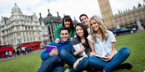 A group of diverse university students sitting on the lawn in London, with the Houses of Parliament and a red double-decker bus in the background, illustrating the journey of alternative pathways like a UK Foundation Year.