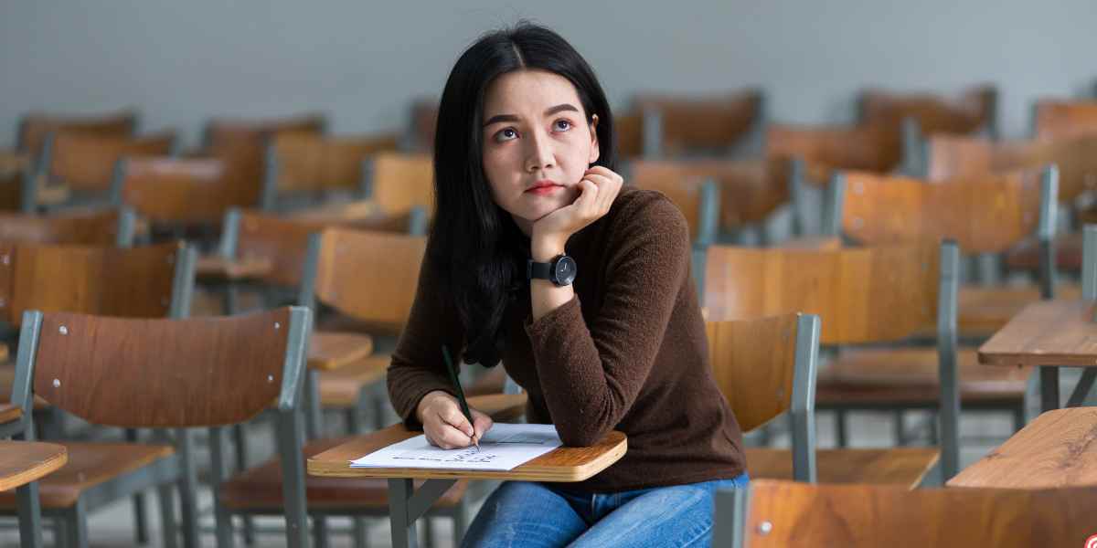 A thoughtful female student sitting alone at a desk in an empty lecture hall, holding a pencil, symbolizing an estranged student contemplating financial options and independent status for university funding.