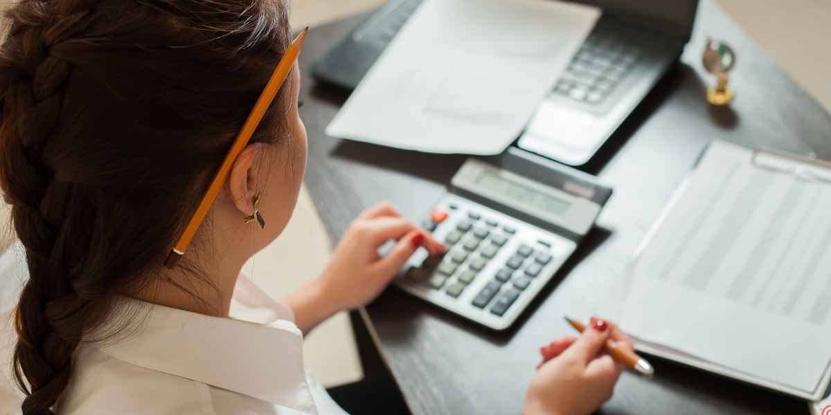Student using a calculator and pen at a desk with study papers, calculating UCAS tariff points and grades.